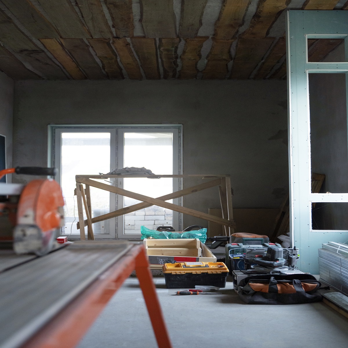 Room under construction with exposed ceiling joists, a tile saw, open toolbox and stacked drywall