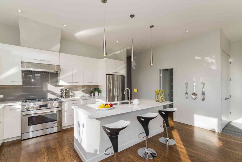 White gloss kitchen with a stainless range, grey tile backsplash and quartz island with bar stools