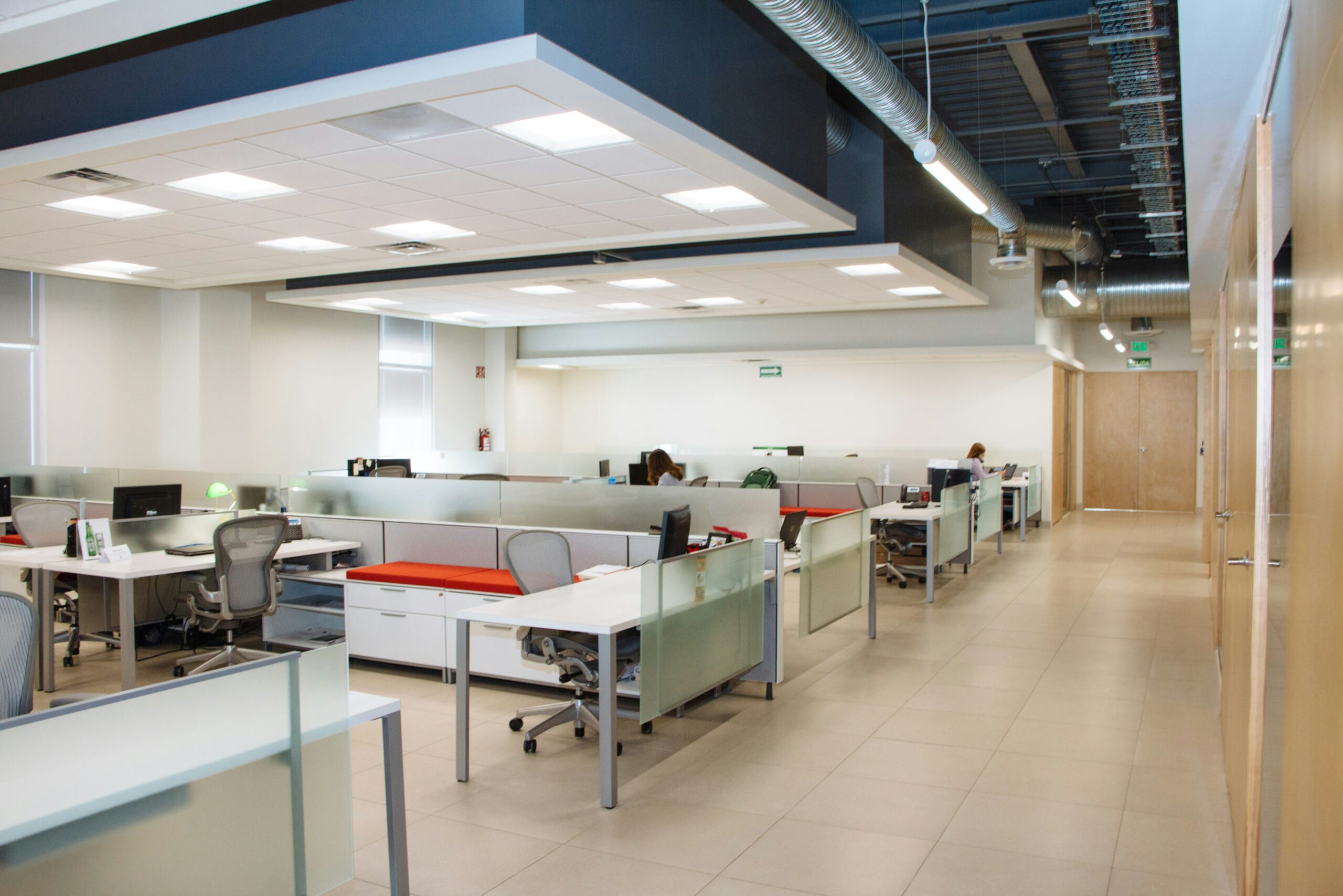 Open-plan office with white desks, glass-partition cubicles, mesh task chairs and exposed ceiling ductwork