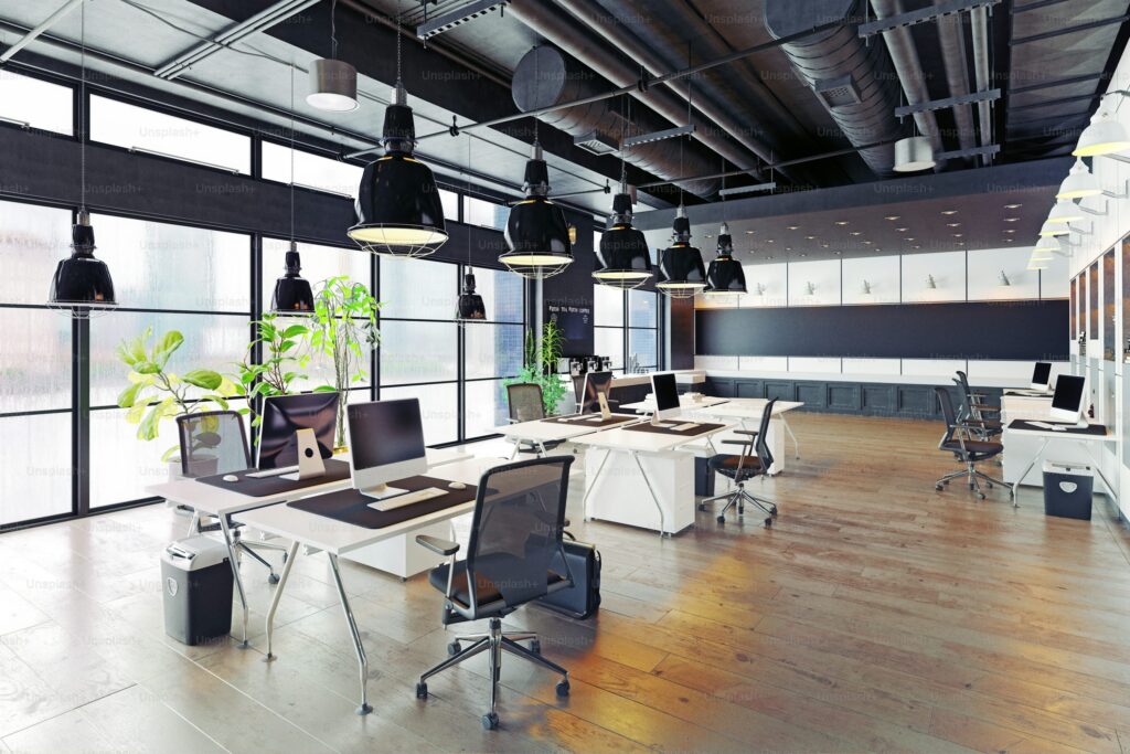 Open-plan office with white desks, black pendant lights, exposed ductwork and wood plank flooring